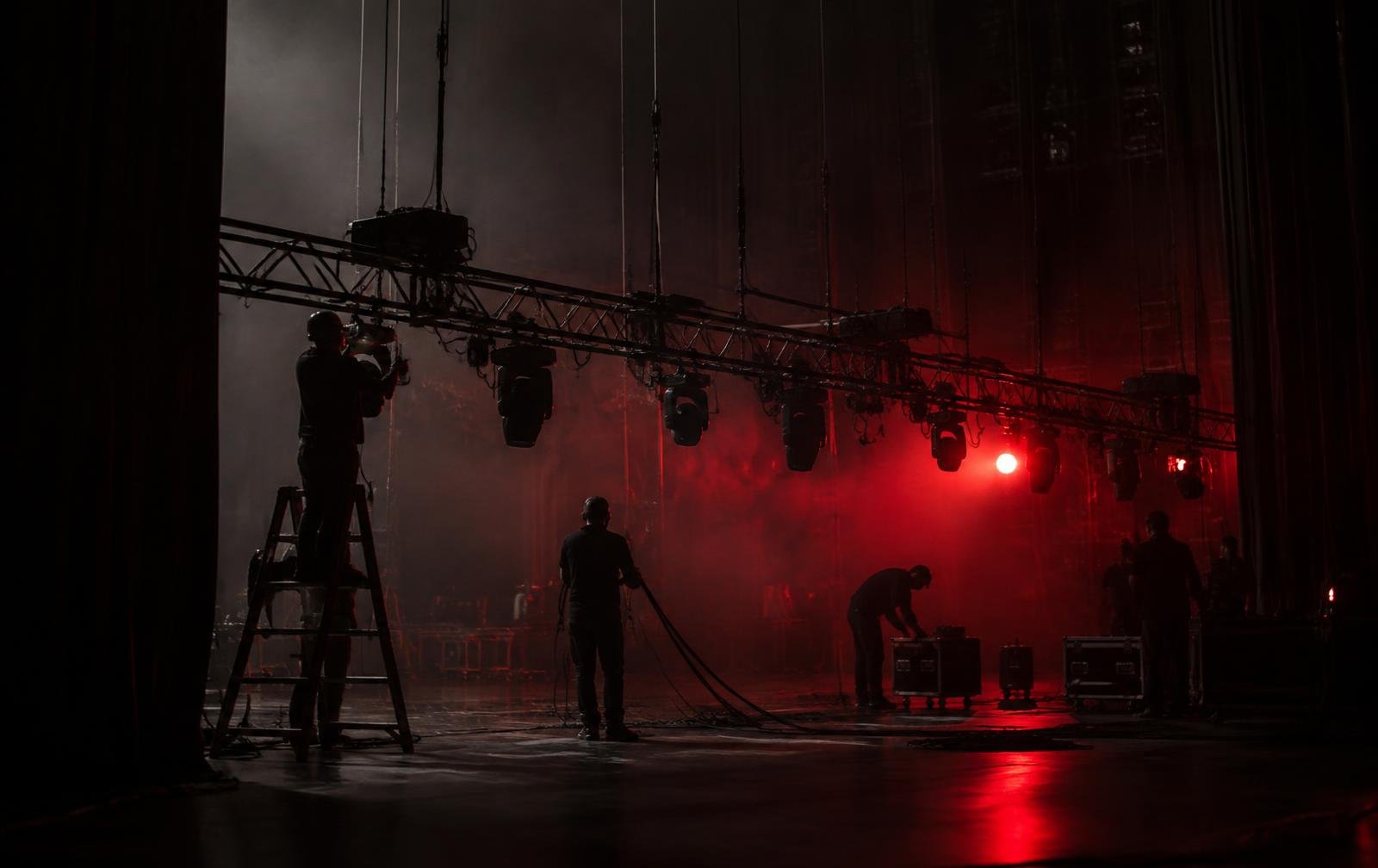 Crew rigging stage lights in a dark theatre before the event